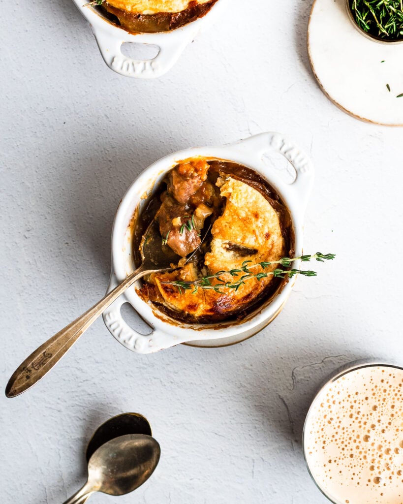 Individual beef and stout pie baked in a ramekin garnished with fresh thyme.