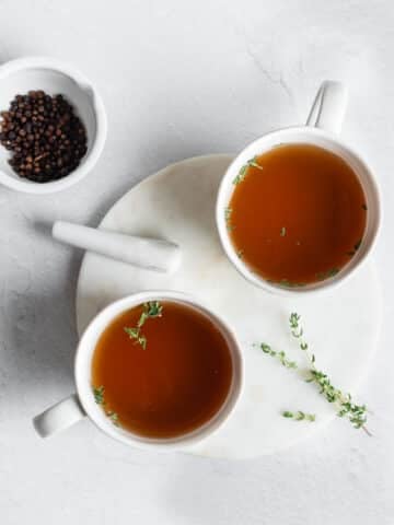Bone broth in mugs and garnished with fresh thyme