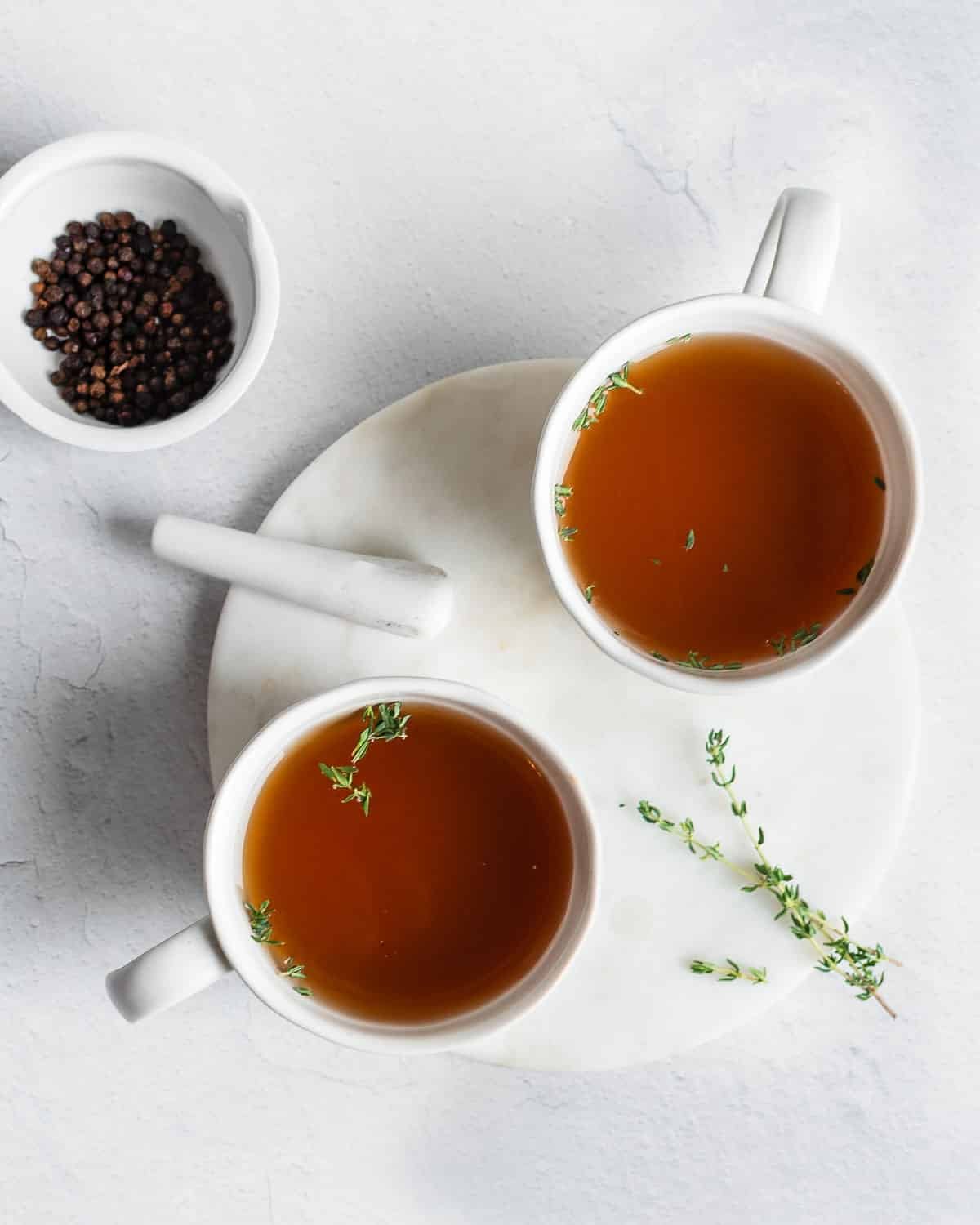 Bone broth in mugs and garnished with fresh thyme