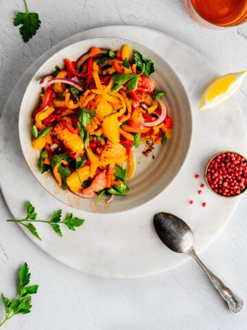 Bell Pepper Salad on an earthenware plate next to a lemon wedge and pinch bowl filled with pink peppercorns