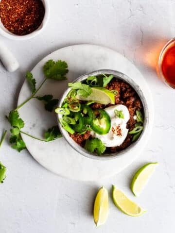 Bison chili in a stoneware bowl garnished with jalapenos, sour cream, green onions, and lime