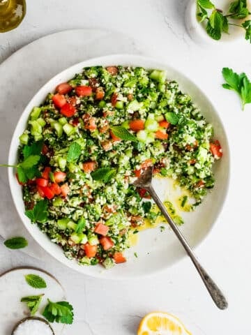 Cauliflower tabbouleh in a white bowl, garnished with mint, lemon and parsley
