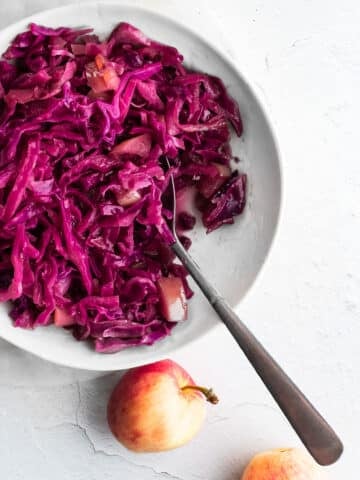 cider-braised cabbage in a white bowl, apples in background