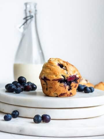 Einkorn blueberry muffin on white surface, milk and blueberries in background.