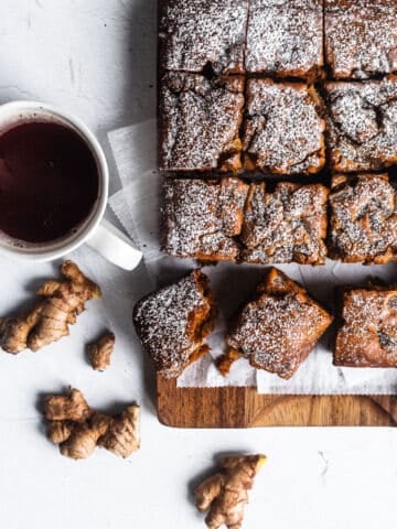 einkorn gingerbread cut into squares and served on a wooden cutting board along with a mug of tea