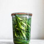 Garlic scapes in clear glass jar on plain background