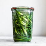 Garlic scapes in clear glass jar on plain background