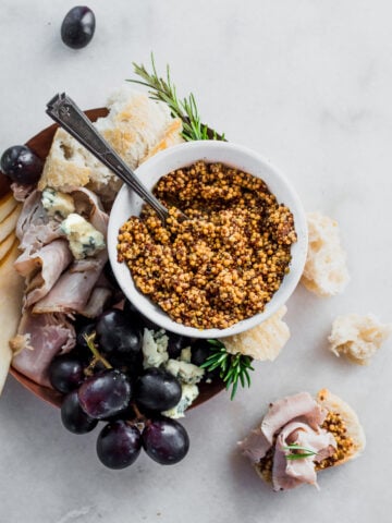 fermented mustard in a small bowl next to grapes cheese crackers and rosemary