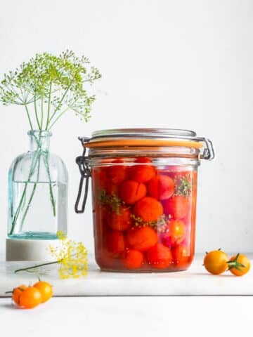 Fermented cherry tomatoes in a clip-top jar, with dill flowers in the background
