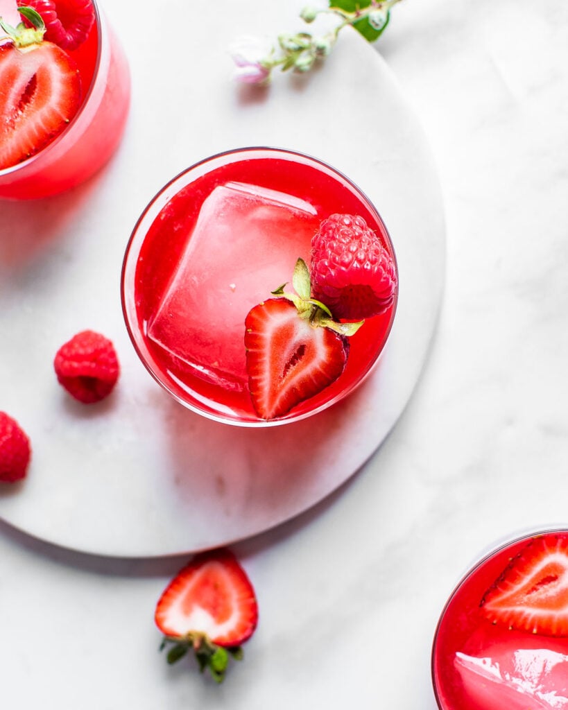 Fruit kvass in three glasses garnished with ice, strawberry and raspberry