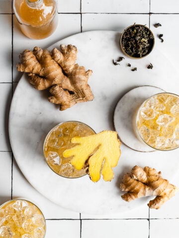 ginger kombucha in glasses of ice garnished with fresh ginger