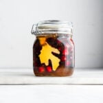 Fresh cranberries and sliced fresh ginger in a honey-filled fido jar on a marble surface