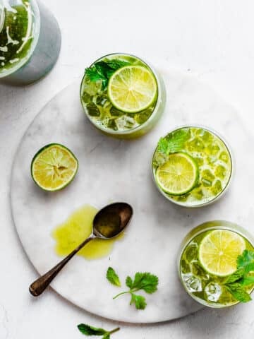 three glasses of herbal limeade on garnished with lime, mint and cilantro