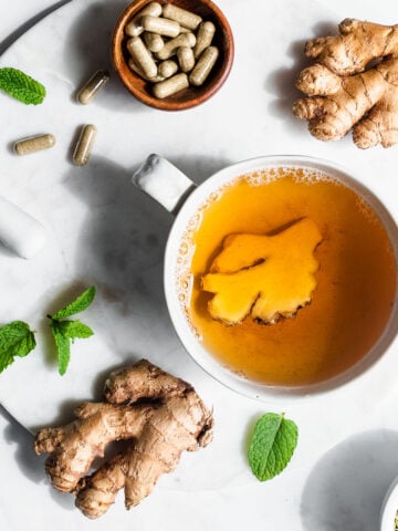 Ginger tea on a marble surface next to sprigs of mint and herbal supplements