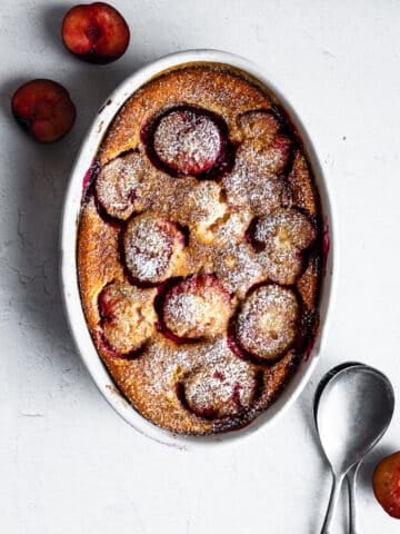 Plum clafoutis in white casserole dish on white surface