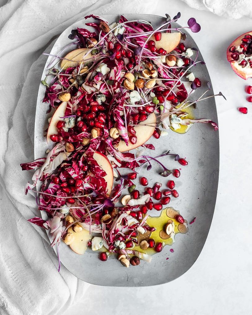 Radicchio salad with pomegranate arils, apples and hazelnuts on a pewter plate.