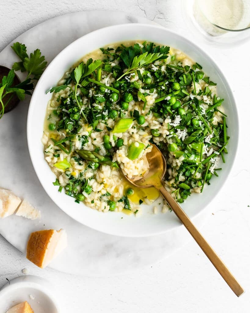 Risotto Primavera (spring risotto) in a white bowl garnished with peas, asparagus and fresh herbs.