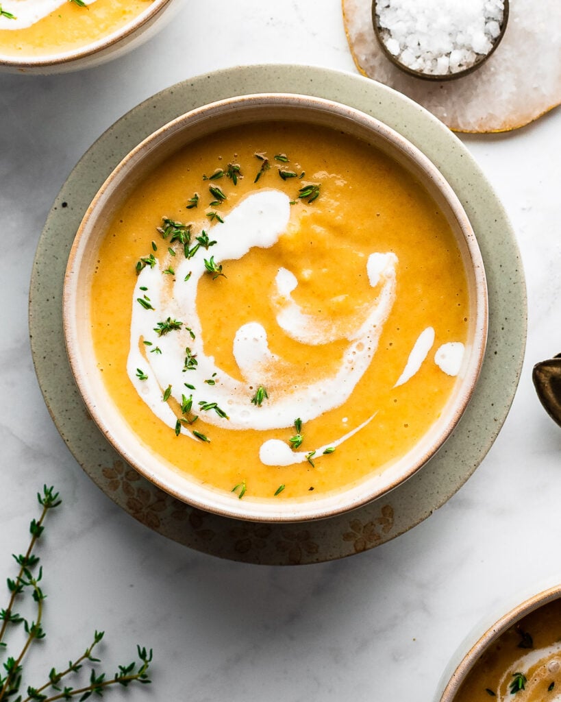 Root vegetable soup in an earthenware bowl, garnished with fresh cream and thyme