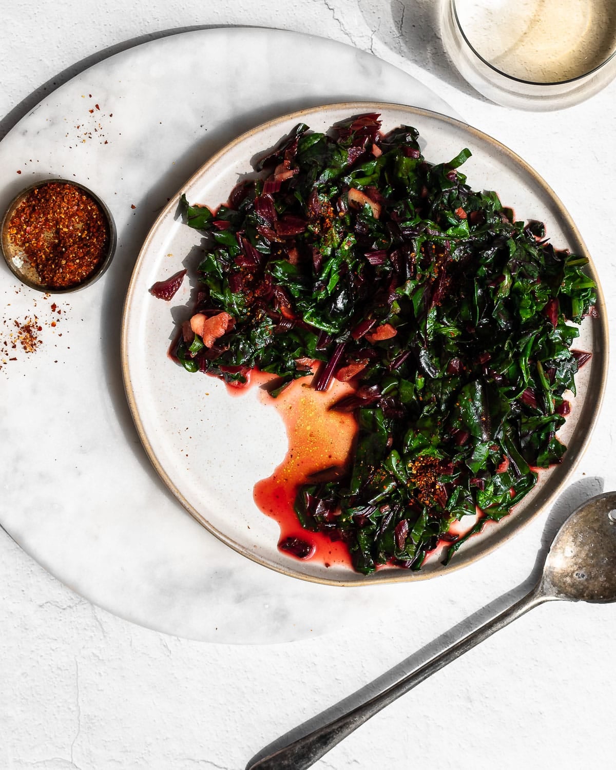 Sauteed greens with garlic on white plate set on white marble surface.