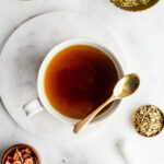 Herbal tea in a white mug with a golden spoon next to small bowls filled with passionflower and rose slightly out of frame