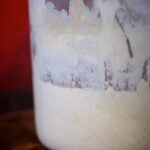 Sourdough starter in a glass jar in front of a red background