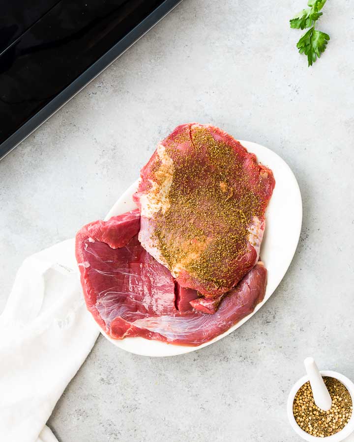 Sprinkling flank steak with cumin, coriander and sea salt on a plate.