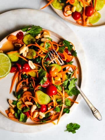 Thai salad with carrots, tomatoes, cucumbers, and peanuts on a plate garnished with lime.