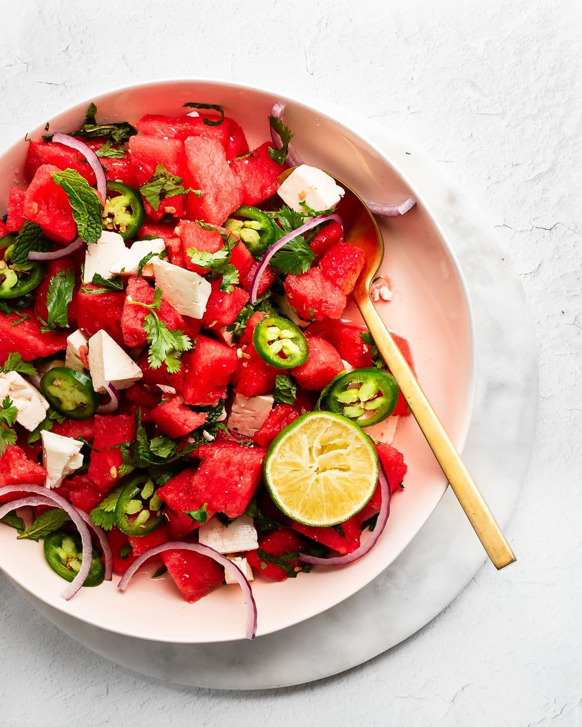 Watermelon and feta salad in a pink bowl garnished with jalapenos, lime and herbs